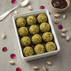 Pistachio truffles in a white dish on a wooden surface with pistachios and Gulkand.